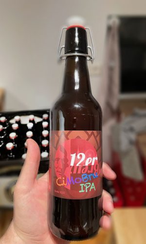 Eine Hand die eine Bierflasche des 12er Brew IPA hält. Im Hintergrund eine Kiste voller Bierflaschen.